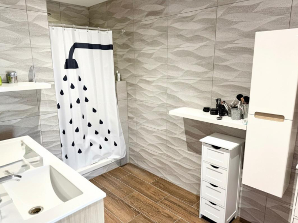 Salle de bain moderne avec douche, lavabo et rangement.