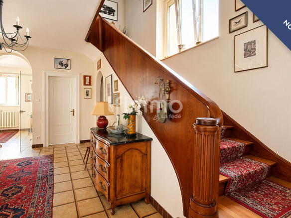 Intérieur d'une maison bourgeoise avec un escalier central en bois et des décorations murales.