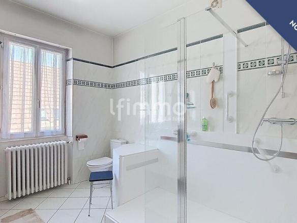 Salle de bain moderne avec douche et baignoire, carrelage blanc et fenêtre lumineuse.
