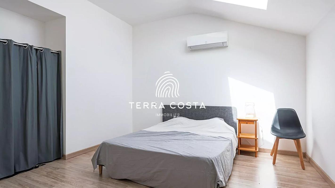 Chambre d'un domaine avec lit, table de nuit et chaise, lumière naturelle entrant par une fenêtre.