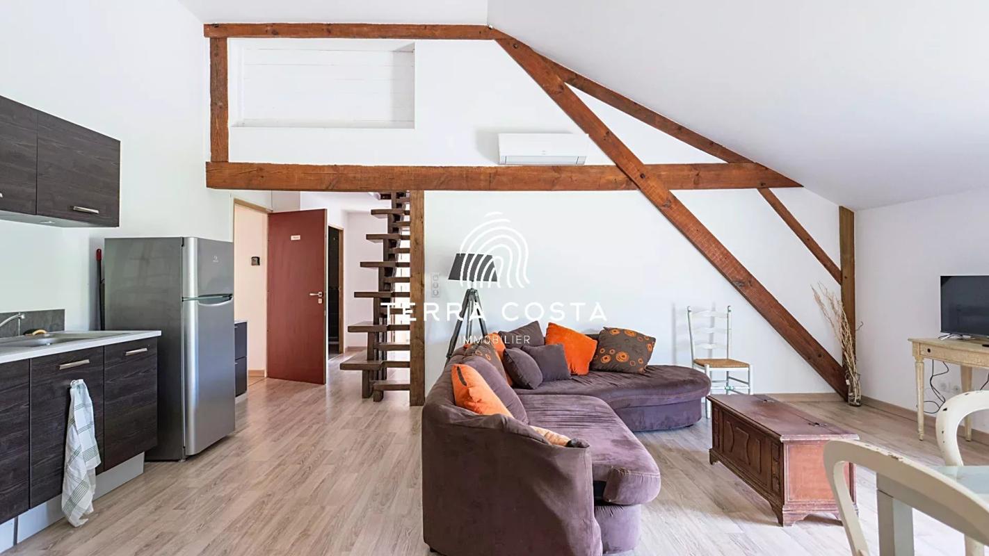 Intérieur d'un espace de vie moderne avec un canapé, une cuisine et des poutres apparentes.