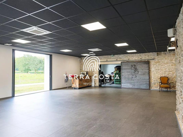 Intérieur d'un espace moderne avec des murs en pierre et un sol carrelé, ouvert sur un parc.