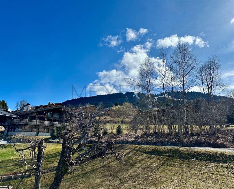 Chalet à Megève Vue d'un chalet à Megève avec des arbres et des montagnes en arrière-plan sous un ciel bleu.