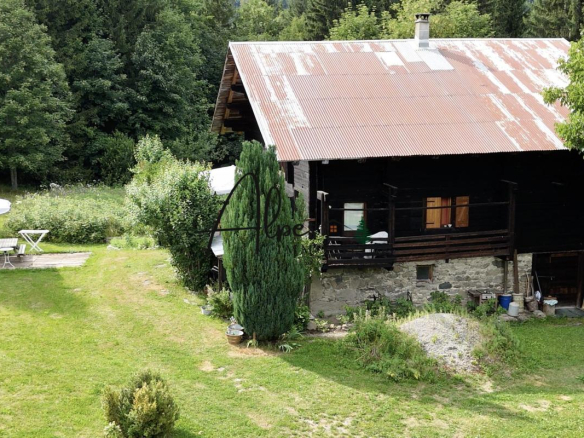 Chalet d'alpage en bois avec toiture en métal, entouré d'arbres et de verdure à La Clusaz.