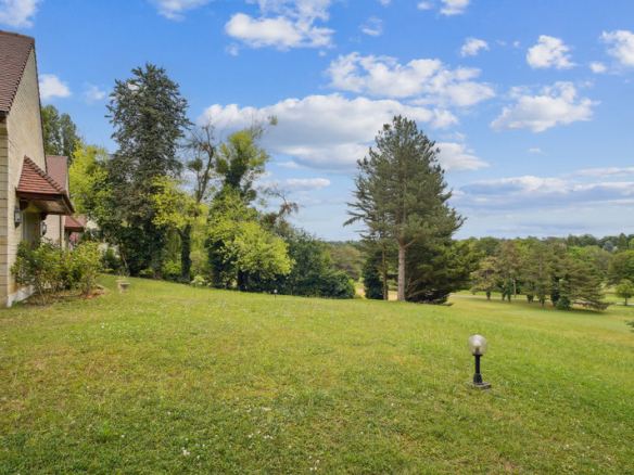 Vue d'un jardin verdoyant avec des arbres et un parcours de golf en arrière-plan.