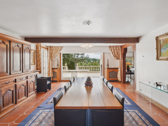Intérieur d'une salle à manger élégante avec une grande table et des fenêtres donnant sur un paysage verdoyant.
