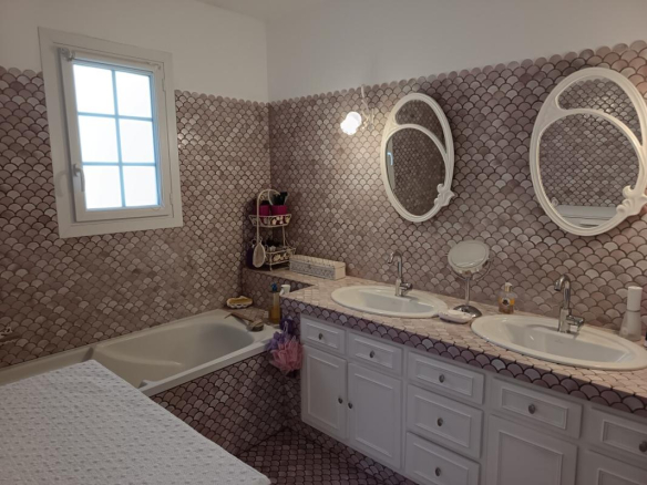 Salle de bain moderne avec baignoire et double vasque, carrelage en mosaïque rose.