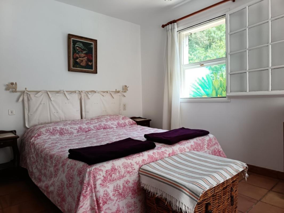 Chambre d'une villa traditionnelle à Toulon, avec lit et fenêtre donnant sur un jardin.