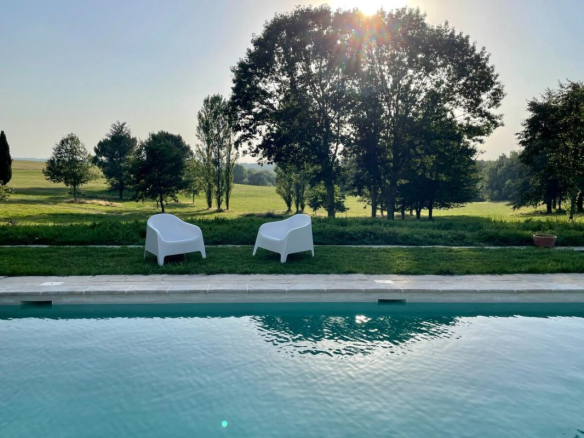 Vue sur une piscine avec des chaises blanches et un parc verdoyant en arrière-plan.