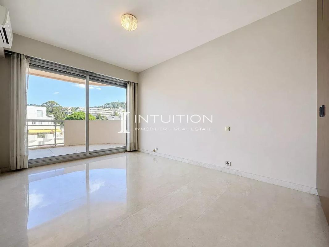 Interior of a bright apartment with a marble floor and a large bay window opening onto a balcony.