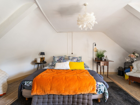Chambre d'une maison avec lit double, décorée de fleurs et d'un plaid orange.