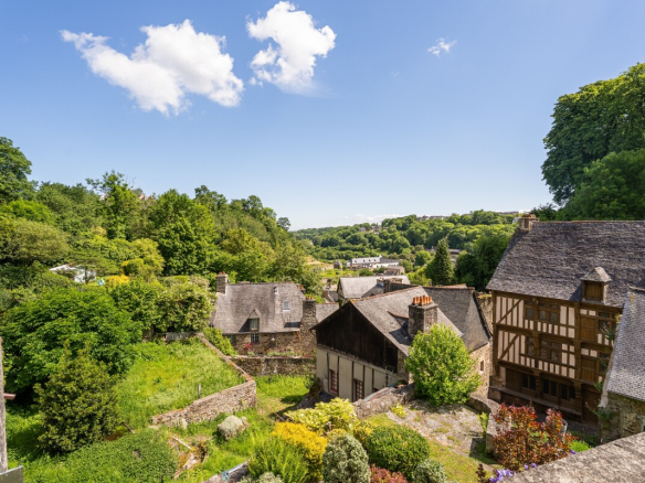 Vue panoramique sur un jardin et des maisons en pierre à Dinan, avec un paysage verdoyant en arrière-plan.