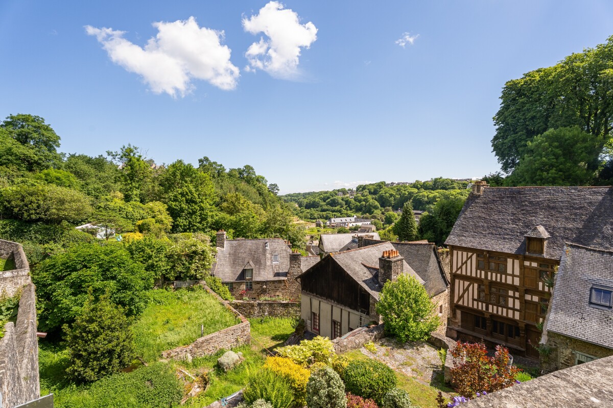 Vue panoramique à Dinan Vue panoramique sur un jardin et des maisons en pierre à Dinan, avec un paysage verdoyant en arrière-plan.