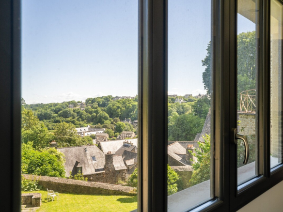 Vue panoramique sur la Rance depuis une maison en pierre à Dinan, avec jardin et maisons en arrière-plan.