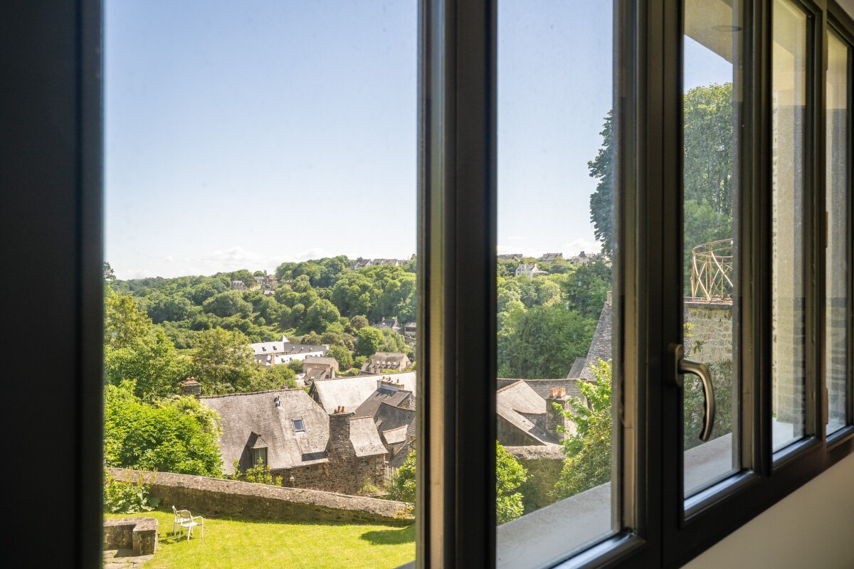 Vue sur la Rance depuis Dinan Vue panoramique sur la Rance depuis une maison en pierre à Dinan, avec jardin et maisons en arrière-plan.