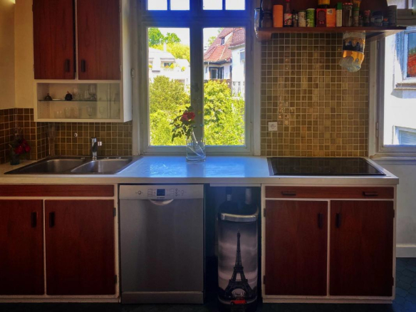 Cuisine lumineuse avec vue sur un parc, meubles en bois et fenêtre ouverte.