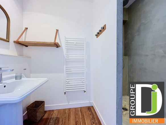 Salle de bain moderne avec lavabo et porte-serviettes, murs en plâtre et sol en bois.