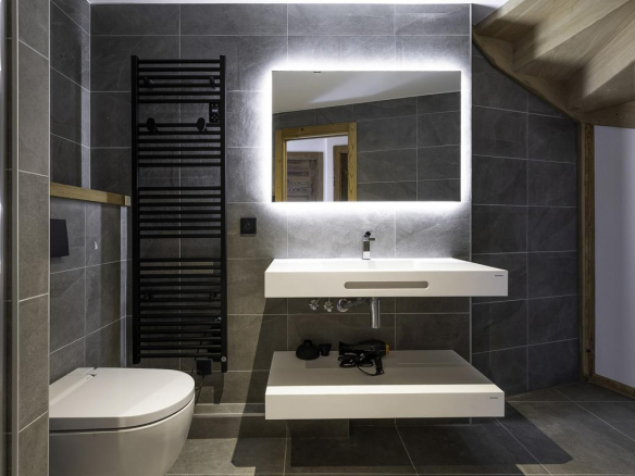 Salle de bain moderne avec lavabo suspendu et douche, carrelage gris, miroir lumineux.