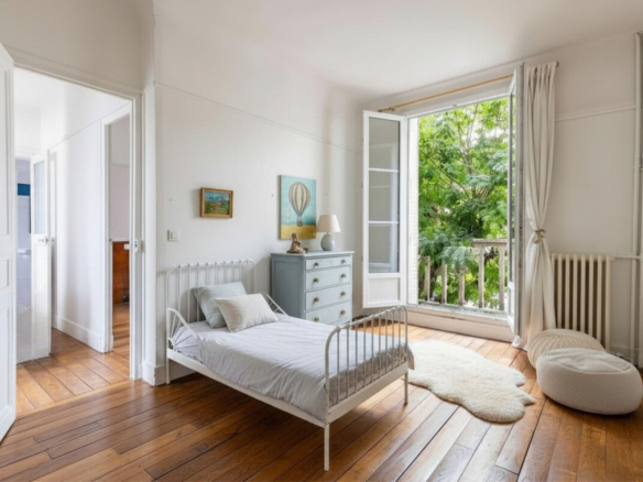 Bright room with single bed, window opening onto a garden, wooden parquet floor.