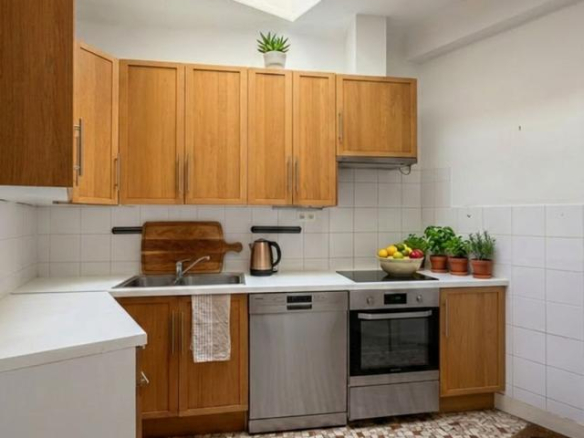 Modern kitchen with wooden furniture and mosaic floor, lit by a skylight.