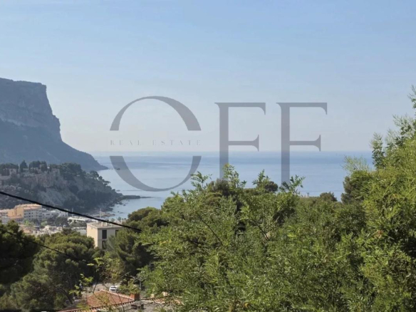 Panoramic view of the sea and hills from Cassis, with trees in the foreground.