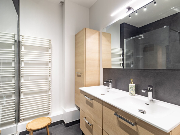 Salle de bain moderne avec double vasque et miroir, radiateur et douche en verre.