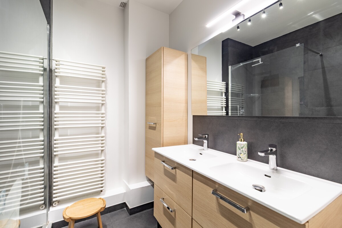 Salle de bain d’un appartement à Paris Salle de bain moderne avec double vasque et miroir, radiateur et douche en verre.