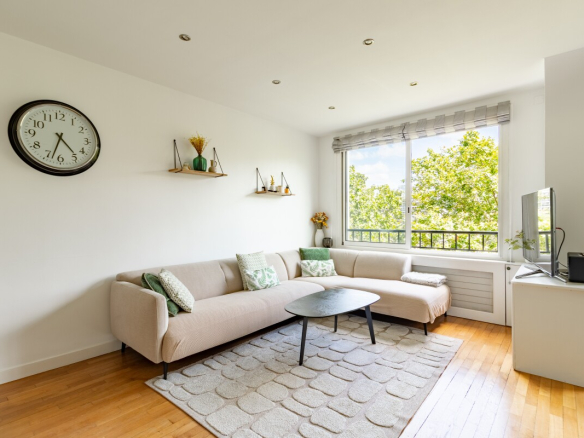 Salon lumineux d'un appartement à Paris avec canapé et télévision.