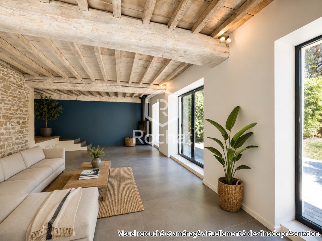 Intérieur d’une maison rénovée à Curis-au-Mont-d’Or Intérieur d'une maison rénovée avec salon moderne, murs en pierre et plafond en bois, baies vitrées.