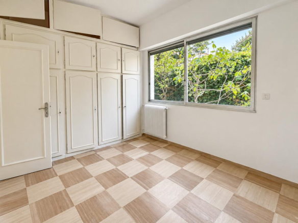 Chambre d'un appartement avec placards intégrés et fenêtre donnant sur un jardin.