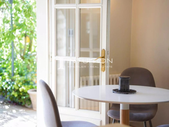 Intérieur d'une villa à Mougins avec une table et des chaises, lumière naturelle et verdure visible à l'extérieur.