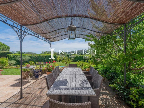 Terrasse d'une villa à Mougins avec table à manger sous un auvent, entourée de verdure.