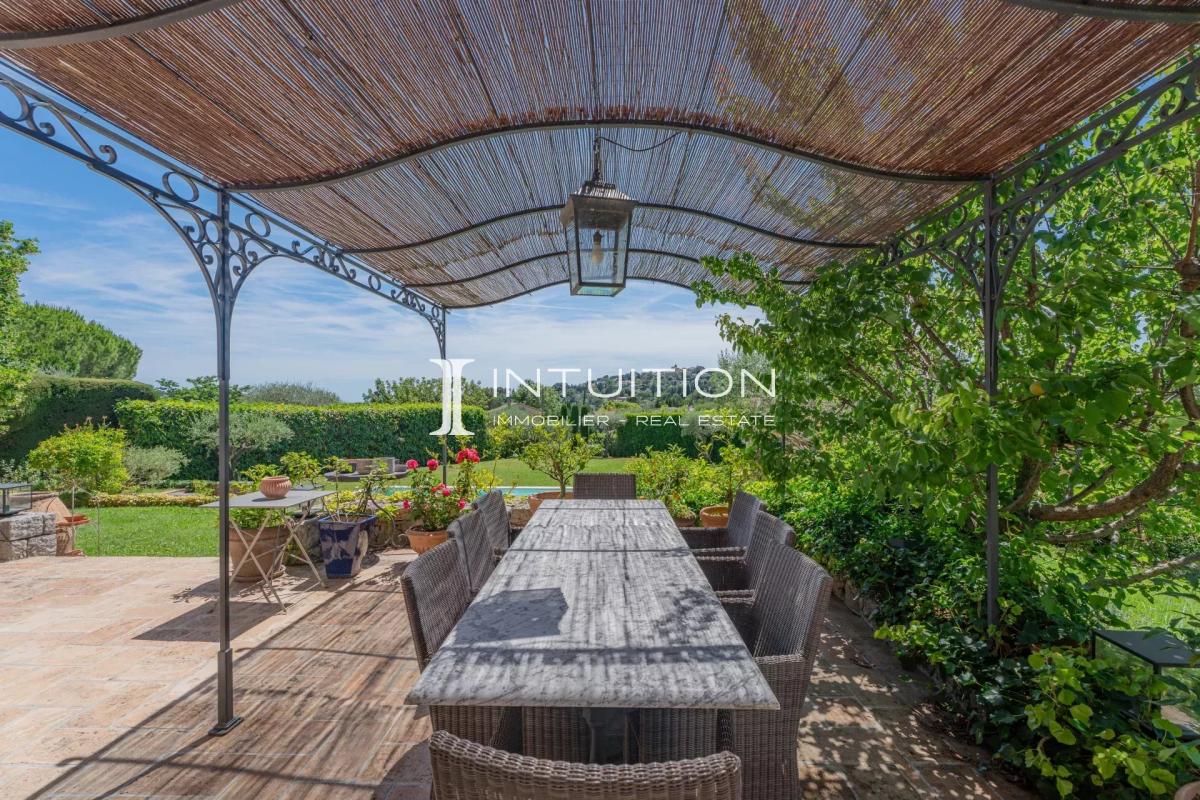 Terrasse de villa à Mougins Terrasse d'une villa à Mougins avec table à manger sous un auvent, entourée de verdure.