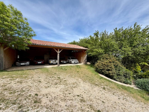 Garage couvert avec plusieurs voitures, entouré de verdure dans un environnement naturel à Mauves.