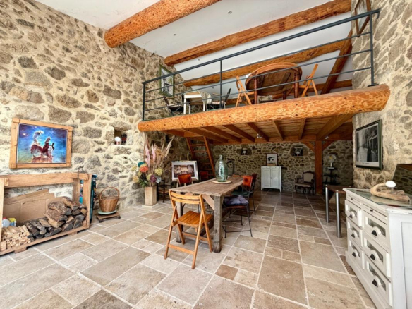 Intérieur d'un corps de ferme rénové avec murs en pierre et mezzanine, mobilier en bois, et espace de vie lumineux.