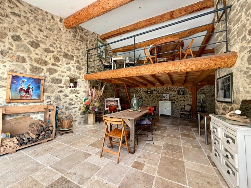 Intérieur d’un corps de ferme rénové Intérieur d'un corps de ferme rénové avec murs en pierre et mezzanine, mobilier en bois, et espace de vie lumineux.