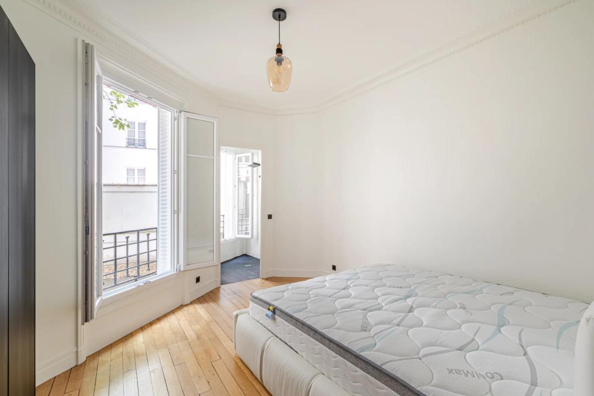 Room in a renovated 75m² apartment in Paris 7th arrondissement, with a bed and windows overlooking a tree-lined courtyard.