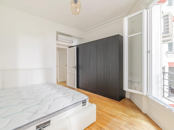 Room in a renovated apartment in Paris with bed and wardrobe, windows opening onto a balcony.