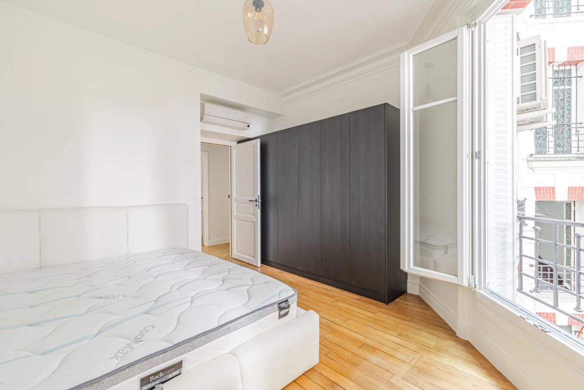 Room in a renovated apartment in Paris with bed and wardrobe, windows opening onto a balcony.