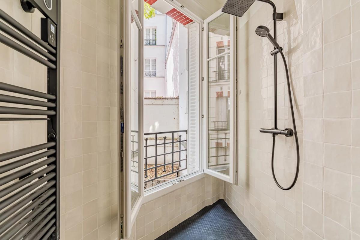 Modern bathroom with shower and window overlooking a tree-lined courtyard.