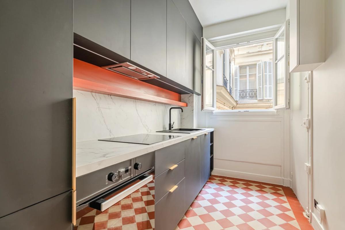Modern kitchen with windows overlooking a tree-lined courtyard in a renovated apartment in Paris 7th arrondissement.