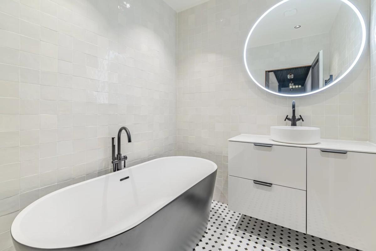 Modern bathroom with bathtub and sink, black and white tiles.