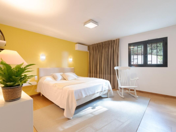 Bright room with yellow walls and double bed, rocking chair and windows.