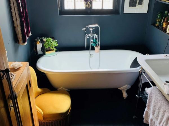 Salle de bain avec baignoire sur pattes et chaise jaune, décorée de plantes et d'œuvres d'art.