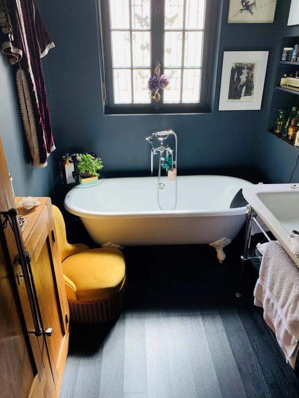 Salle de bain élégante Salle de bain avec baignoire sur pattes et chaise jaune, décorée de plantes et d'œuvres d'art.