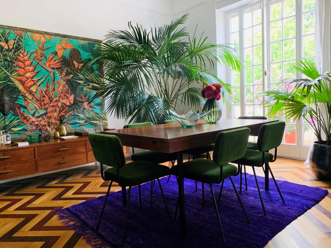 Salle à manger dans un duplex à Strasbourg Salle à manger avec table en bois et chaises vertes, entourée de plantes et d'une grande fenêtre.