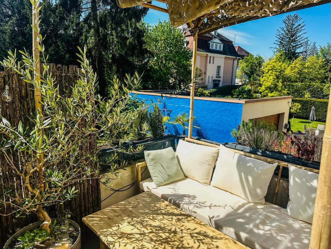 Terrasse du duplex à Strasbourg Terrasse avec canapé et plantes, vue sur jardin et piscine, duplex à Strasbourg.
