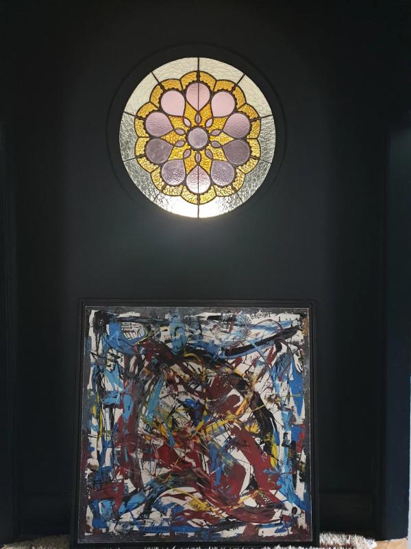 Vitrail et œuvre d’art Vitrail circulaire coloré au-dessus d'une œuvre d'art abstraite dans un intérieur sombre.