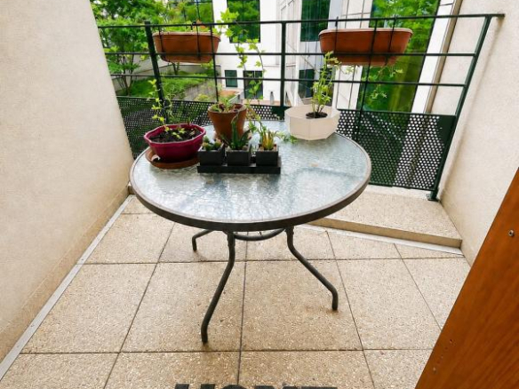 Terrasse d'un appartement avec une table et des plantes, vue sur un bâtiment moderne.