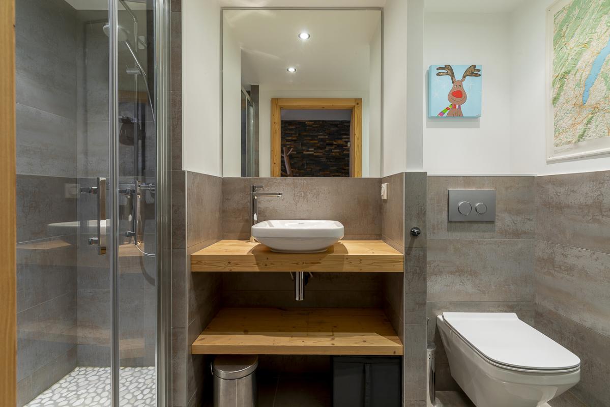 Salle de bain du duplex du Kouria à Avoriaz Salle de bain moderne avec douche, lavabo sur meuble en bois et toilettes.